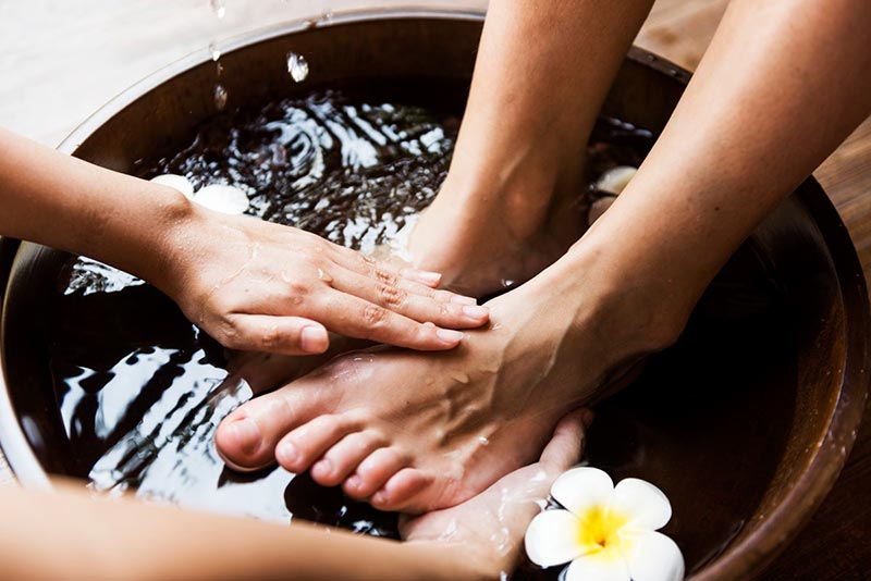 Hands giving a foot massage to a pair of feet in a bowl of water