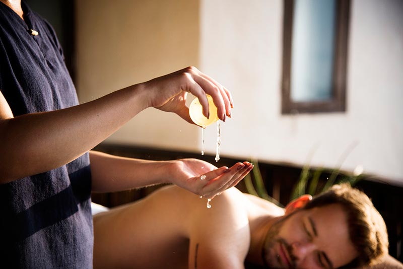 Masseuse preparing massage oil with male lying on massage table awaiting a back massage
